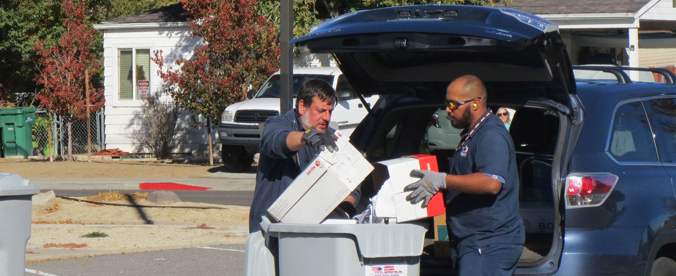 two workers emptying boxes of paper into shredding container