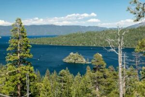 Image of Lake Tahoe, CA showing evergreens and dark blue lake with mountains in the background